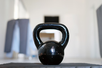 Naklejka na ściany i meble Close up on black iron metal kettlebell griya weight training equipment on the exercise mat on the floor at home in day