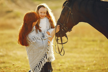 Mother and daughter next to horse. Little girl in a summer field. Family playing with a horse