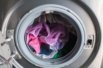 Man taking color clothes from washing machine. A drum of washing machine full of dirty laundry in the bathroom.