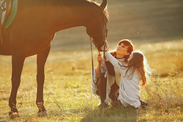 Mother and daughter next to horse. Little girl in a summer field. Family playing with a horse