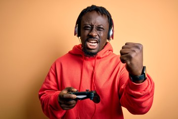 Fototapeta na wymiar Young african american gamer man playing video game using joystick and headphones annoyed and frustrated shouting with anger, crazy and yelling with raised hand, anger concept