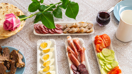breakfast table: chopped vegetables, sliced meat, boiled eggs on long white porcelain plates on a white tablecloth