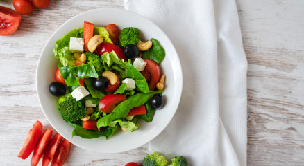 Zenith view close up of salad of spinach, avocado, lettuce, tomatoes, broccoli and black olives on a white table.  