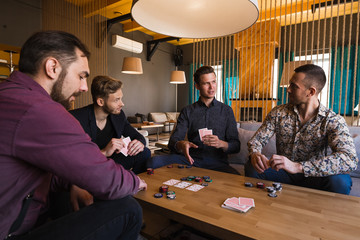 Several men are playing poker in a cafe, holding cards in their hands.