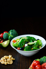 Salad of spinach, avocado, lettuce, tomatoes, broccoli and black olives. Dark photography. 