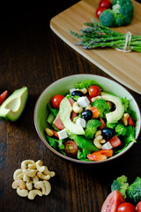 Salad of spinach, avocado, lettuce, tomatoes, broccoli and black olives. Dark photography.