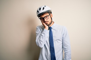 Young businessman wearing glasses and bike helmet standing over isolated white bakground thinking looking tired and bored with depression problems with crossed arms.