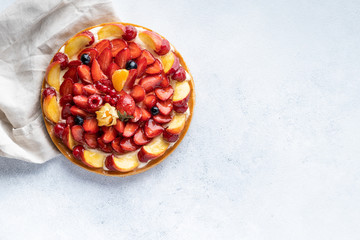 Homemade open tart with strawberries, raspberries, blueberries and grapes on a grey background. Homemade cake. The concept of healthy and delicious food. Top view, copy space.