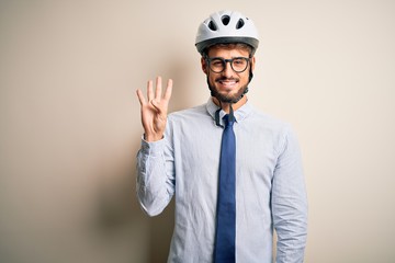 Young businessman wearing glasses and bike helmet standing over isolated white bakground showing and pointing up with fingers number four while smiling confident and happy.