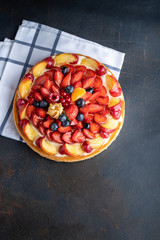 Homemade open tart with strawberries, raspberries, blueberries and grapes on a black background. Homemade cake. The concept of healthy and delicious food. Top view, copy space.