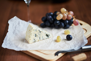 A piece of blue cheese and grapes are on a wooden cutting board.