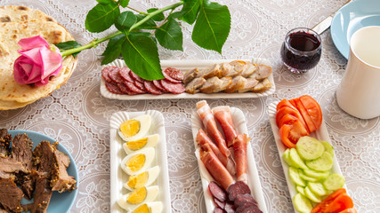 Fototapeta na wymiar breakfast table: chopped vegetables, sliced meat, boiled eggs on long white porcelain plates on a white tablecloth