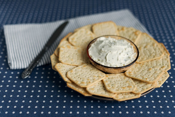 A plate with crackers and curd cheese lying on a polka dot tablecloth.