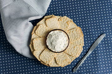 A plate with crackers and curd cheese lying on a polka dot tablecloth.