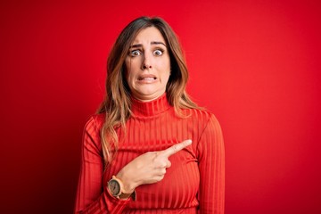 Young beautiful brunette woman wearing casual turtleneck sweater over red background Pointing aside...