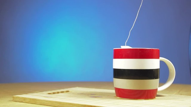 Slow motion shot tea bag is brewed in a white mug. Close up. On a blue background