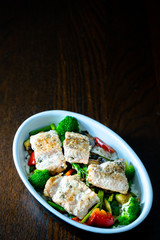 Fuente con salmón salvaje, arroz, esparragos trigueros, brócoli, pimiento rojo y champiñones sobre mesa marrón. Dark photography. Close Up. 