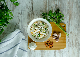 Bol blanco de gulas con gambas, ajos, perejil, guindillas sobre mesa blanca, cenital