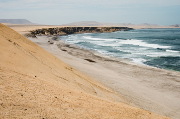 Paisaje costero desértico con una amplia playa y oleaje  en la Reserva Natural de Paracas en Perú