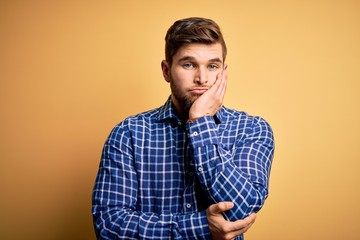 Young blond businessman with beard and blue eyes wearing shirt over yellow background thinking looking tired and bored with depression problems with crossed arms.