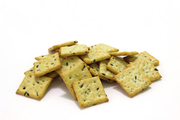 Heap of small square crackers with sesame seeds and flax seeds on a white background.