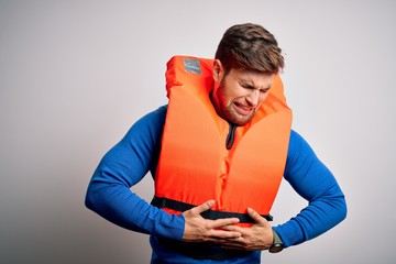 Young blond tourist man with beard and blue eyes wearing lifejacket over white background with hand on stomach because nausea, painful disease feeling unwell. Ache concept.