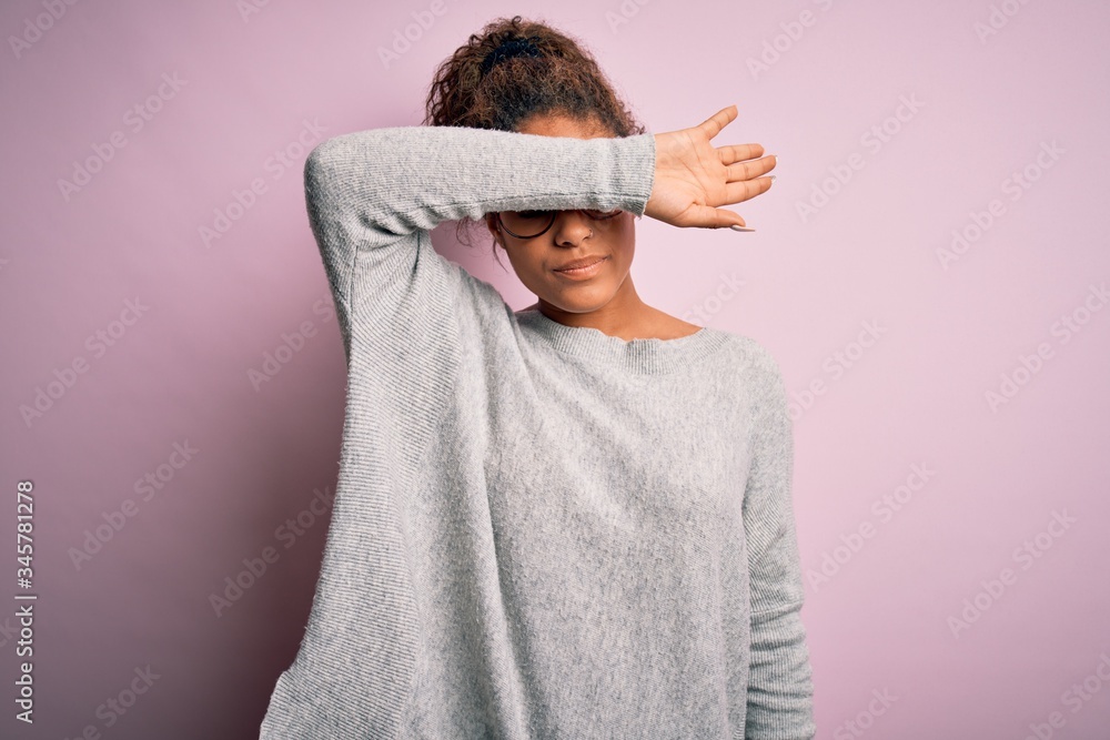 Sticker Young beautiful african american girl wearing sweater and glasses over pink background covering eyes with arm, looking serious and sad. Sightless, hiding and rejection concept