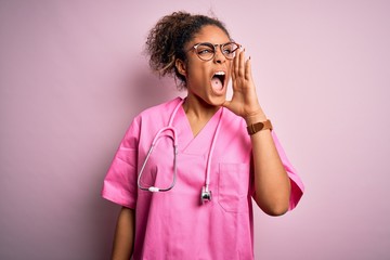 African american nurse girl wearing medical uniform and stethoscope over pink background shouting and screaming loud to side with hand on mouth. Communication concept.