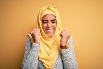 Young beautiful african american girl wearing muslim hijab over isolated yellow background excited for success with arms raised and eyes closed celebrating victory smiling. Winner concept.