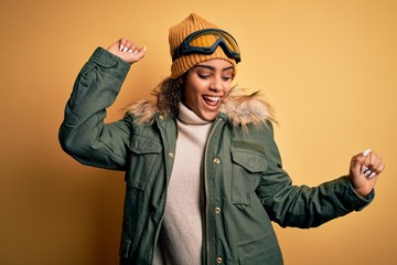 Young african american afro skier girl wearing snow sportswear and ski goggles Dancing happy and cheerful, smiling moving casual and confident listening to music