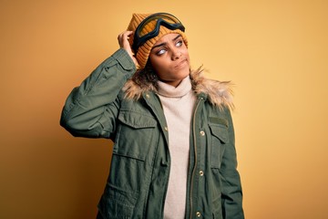 Young african american afro skier girl wearing snow sportswear and ski goggles confuse and wondering about question. Uncertain with doubt, thinking with hand on head. Pensive concept.