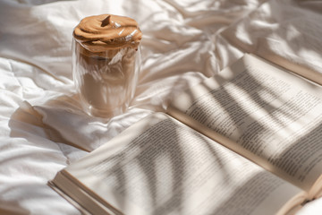 Dalgona coffee and book in bed with sun glare and palm shadows. Horizontal