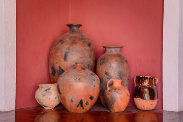 Several clay jugs with a narrow neck against a red wall.