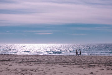 Fototapeta na wymiar Two unrecognizable women walking on empty sandy Mediterranean beach in Benidorm Spain