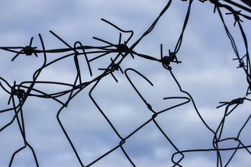 Metal barbed wire against a blue sky background: imprisonment and slavery