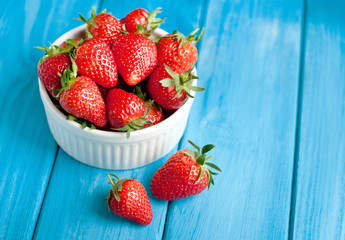 Ripe strawberries in a white bowl on a blue wooden background. Healthy fresh berries.