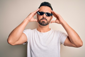 Fototapeta na wymiar Young handsome man with beard wearing funny thug life sunglasses over white background suffering from headache desperate and stressed because pain and migraine. Hands on head.