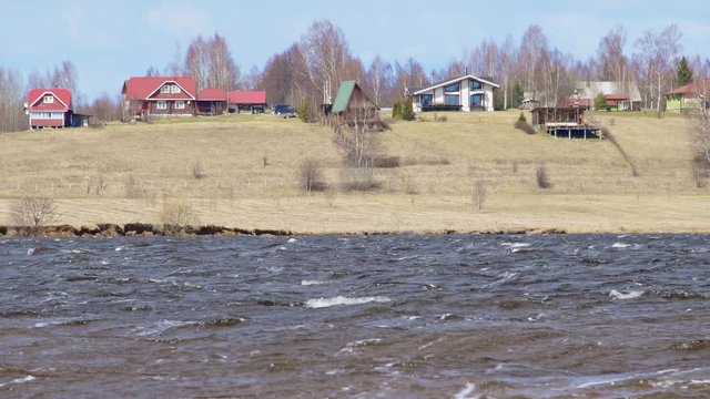 Spring river bank with waves on the river and houses on the shore