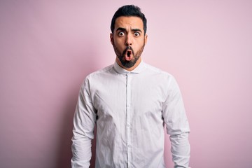 Young handsome man with beard wearing casual shirt standing over pink background afraid and shocked with surprise expression, fear and excited face.
