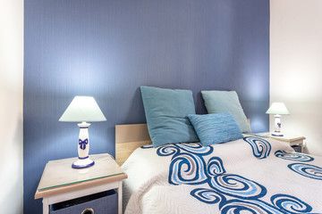 Home modern bedroom in blue marine tones. Lamps shine and headboards.