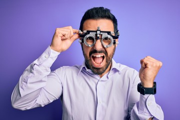 Obraz premium Young handsome optical man with beard wearing optometry glasses over purple background screaming proud and celebrating victory and success very excited, cheering emotion