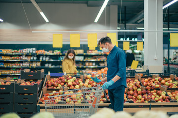 shoppers in protective masks standing in a supermarket at a safe distance