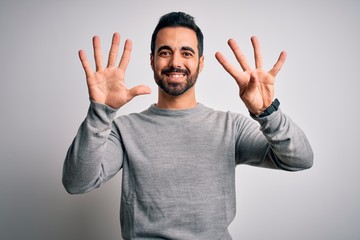 Fototapeta premium Young handsome man with beard wearing casual sweater standing over white background showing and pointing up with fingers number nine while smiling confident and happy.