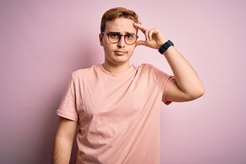 Young handsome redhead man wearing casual t-shirt standing over isolated pink background worried and stressed about a problem with hand on forehead, nervous and anxious for crisis