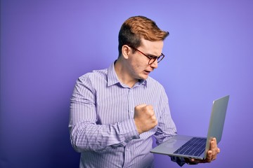 Young handsome redhead businessman working using laptop over purple background annoyed and frustrated shouting with anger, crazy and yelling with raised hand, anger concept