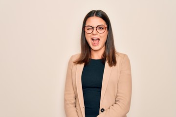 Obraz premium Young beautiful brunette businesswoman wearing jacket and glasses over white background winking looking at the camera with sexy expression, cheerful and happy face.
