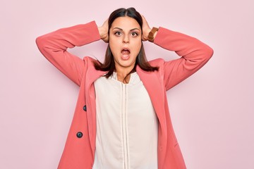 Young beautiful brunette businesswoman wearing elegant jacket over isolated pink background Crazy and scared with hands on head, afraid and surprised of shock with open mouth