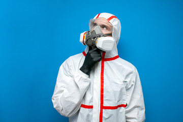 disinfector man in a protective suit thinks and looks at a place for text on a blue isolated background, disinfection service worker