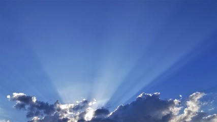 Fototapeta na wymiar sun rays bursting forth from behind clouds against a blue sky