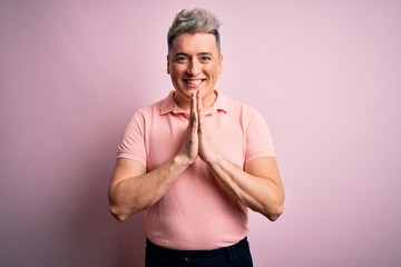 Fototapeta premium Young handsome modern man wearing casual pink t-shirt over isolated background praying with hands together asking for forgiveness smiling confident.